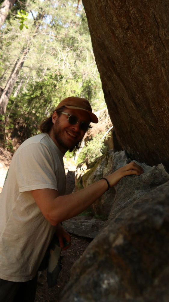 Me, with a cap and glasses touching a rock and smiling 