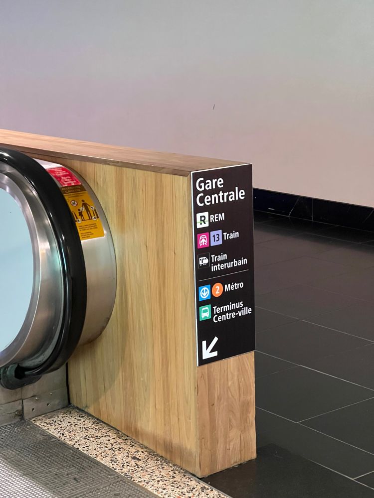 Small sign pointing down to the left towards an escalator, to Gare Centrale, with connecting trains and bus services