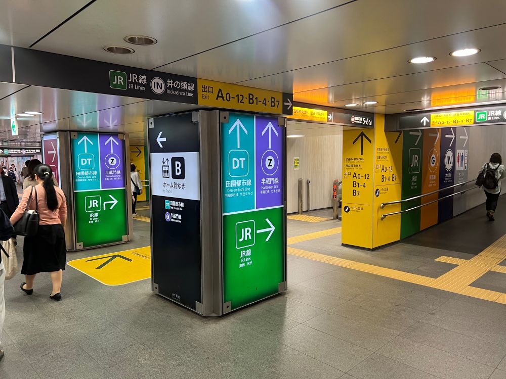 A pillar with a lit up colourful sign, and signs attached to the ceilings pointing to exits