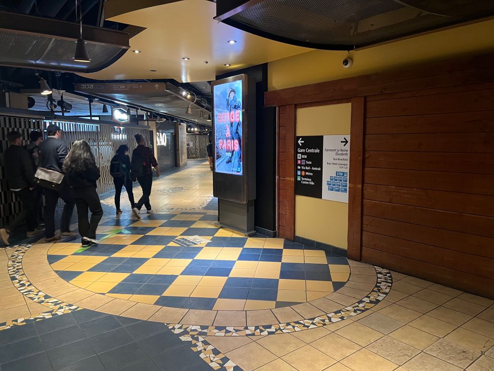 Large plastic placed on false door, pointing to the left to Gare Centrale with connections (REM, exo train, VIA, Amtrak, Métro, and Terminus Centre-ville) and outside to the right, to the hotel, and connecting buses