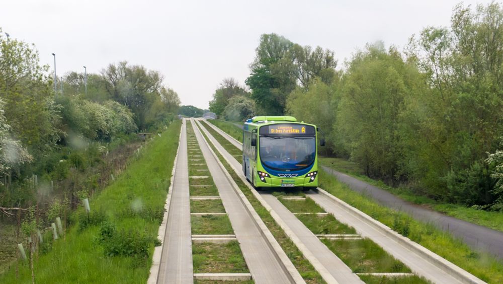 Cambridgeshire Guided Busway, with grass in the middle of the track, and a green bus travelling along it. 