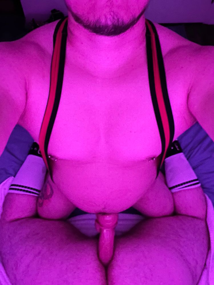 my boyfriend in a singlet fucking me with a large dildo inserted in my ass, with the shaft sticking out and the head buried in my hole. Photo taken from above, showing bf’s jaw and torso, and my ass, thighs and legs. I’m wearing athletic knee high socks and leather straps.