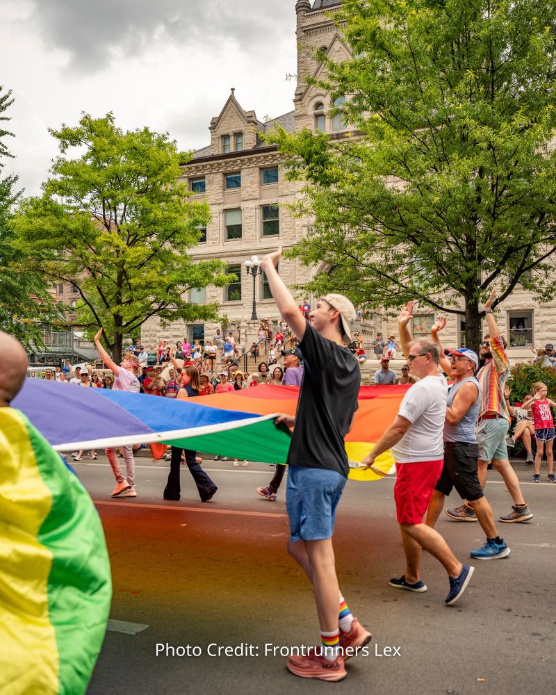 Group of lgbtq activists in July 4th parade walking down the street holding an enormous pride flag and waving