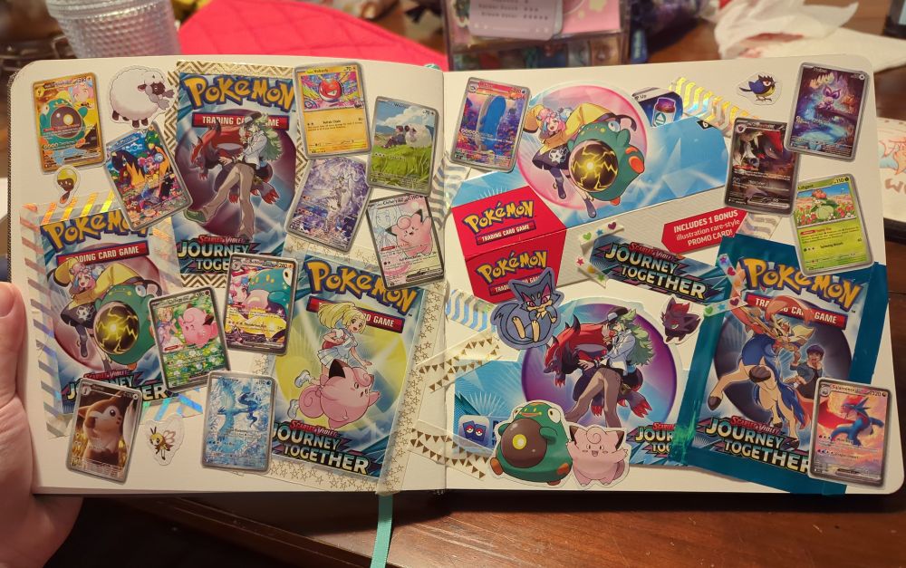 A scrapbook spread consisting of cut up Pokemon card packaging from the Journey Together expansion taped down with washi tape. Cut outs of cards and Pokemon from the Elite Trainer Box booklet are glued on top. 
Left page: 
pack art of N (held down with gold and white zigzag washi tape), Iono (held down with holographic and white striped washi tape), and Lillie (held down with white with gold star washi tape). Cards from left to right: iono's bellibolt (gold), iono's kilowattrel IR, iono's voltorb, hop's wooloo IR, N's reshiram IR, Lillie's Clefairy FA, furret IR, Lillie's Clefairy SIR, iono's bellibolt SIR, articuno IR
Pictures of wooloo, tadbulb, and ribombee
Right page: booster box flaps of iono and N , pack art of hop (held down with shiny blue tape). Cards from left to right: wailord IR, small cutout of N's PP Up hidden behind the iono flap, n's zoroark SIR, noibat IR, Lilligant, salamence IR
Cutouts of bellibolt, Clefairy, zorua, and rookidee, and a logo from a pack
A sticker of purrloin 