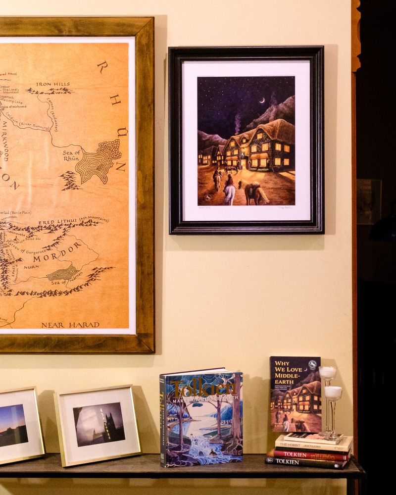 My print of the Prancing Pony Inn framed and hung on the wall next to a huge Middle-earth map. Several Tolkien related books sit on a shelf below.