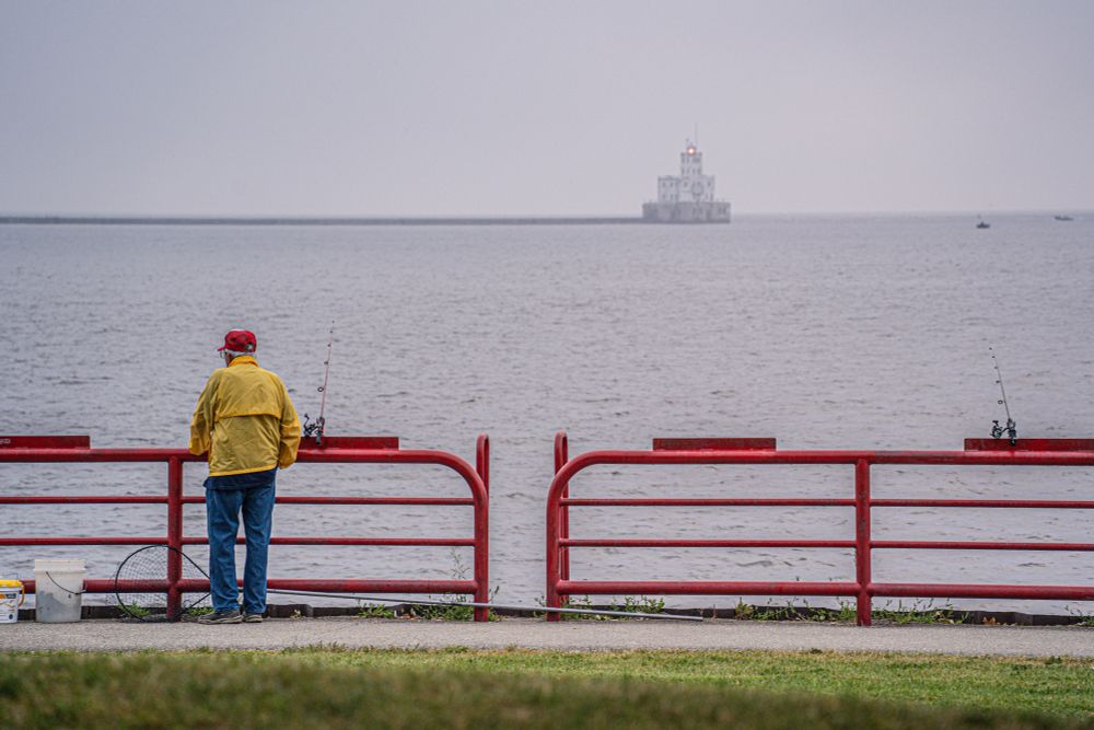 A man in a yellow jacket and blue jeans stares out at Lake Michigan from Lakeshore State Park in Milwaukee, WI. 