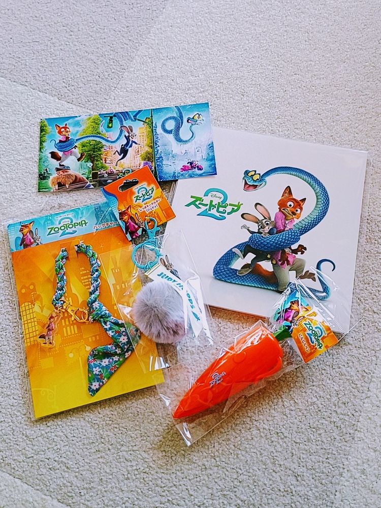ズートピア2グッズ。左上から、入場特典のポストカード、パンフレット、ジュディのしっぽキーホルダー、バッグチャーム、にんじんペン。