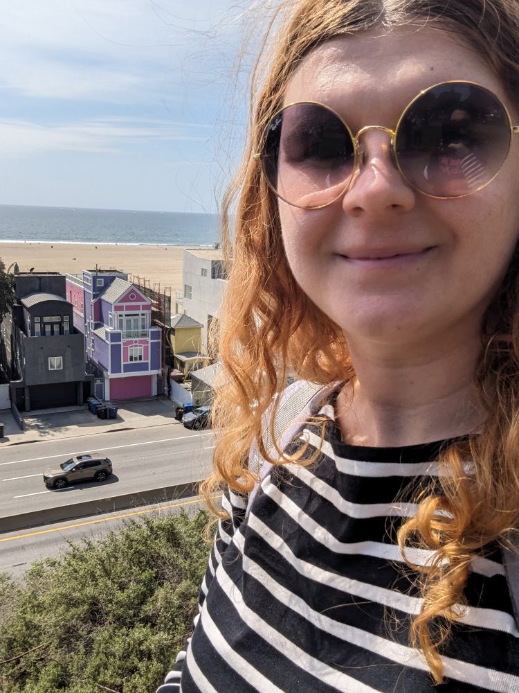 A selfie of a woman standing in front of a completely black house with a pink and purple house right next to it