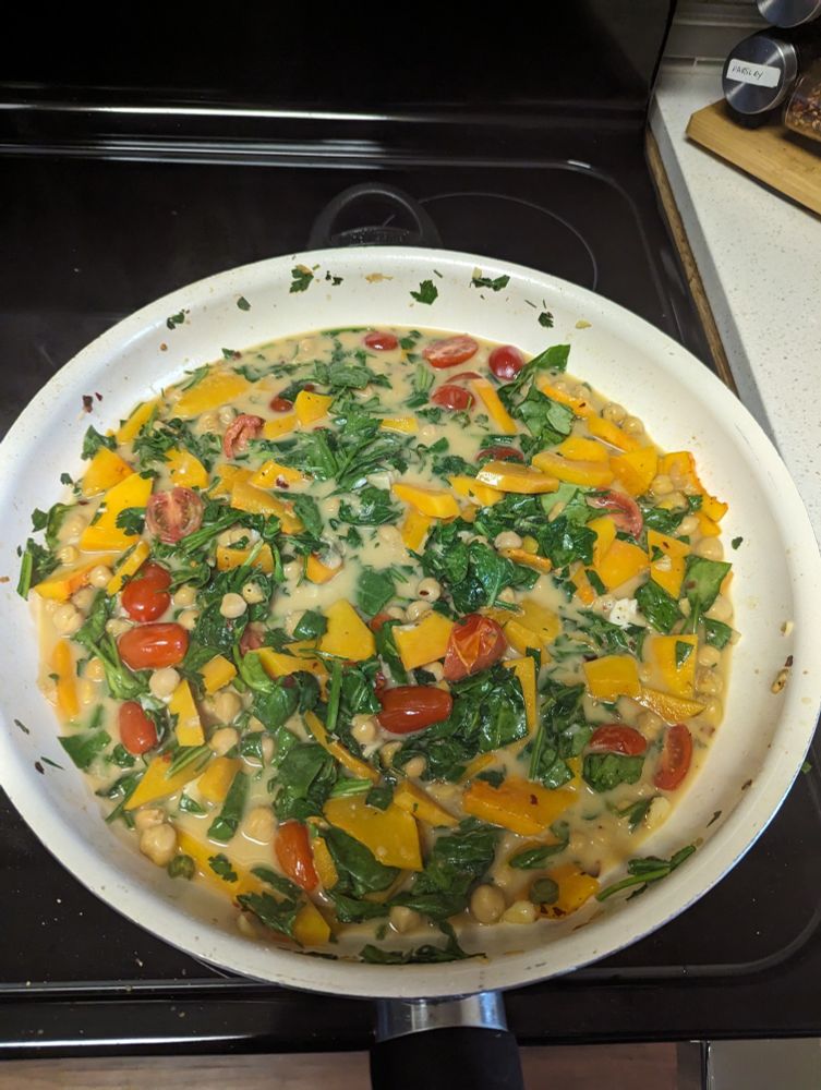 A big pan filled with pumpkin, chickpeas, cherry tomatoes, spinach, parsley and dill and creamy sauce