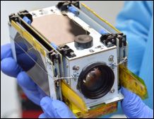An image of a pico satellite fitting in the hands of a person. The satellite has a small camera and small antennas.