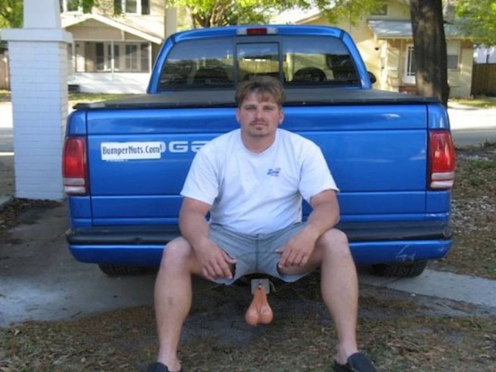 Idiot man sitting on his blue truck’s hitch so the hanging balls on the hitch look like they could be his balls (to make up for his tiny dick, probably)