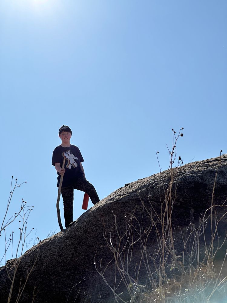 A boy standing on a boulder, sun behind