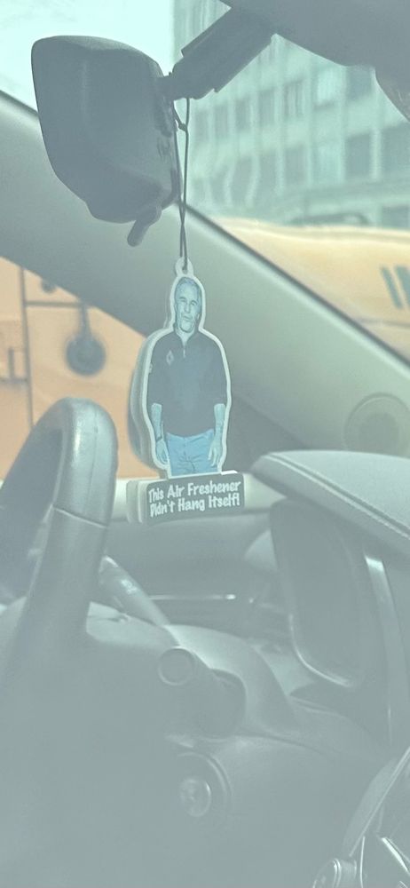 A car parked outside MDC Brooklyn with an air freshener of Jeffrey Epstein that reads, “This Air Freshener Didn’t Hang Itself.”