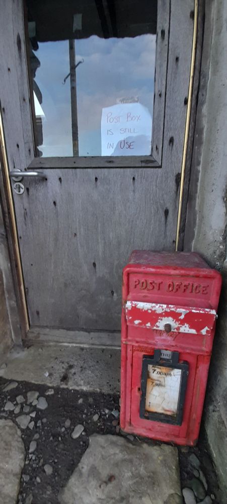 A doorway with a postbox and a sign on the door saying 'Post Box still in use'