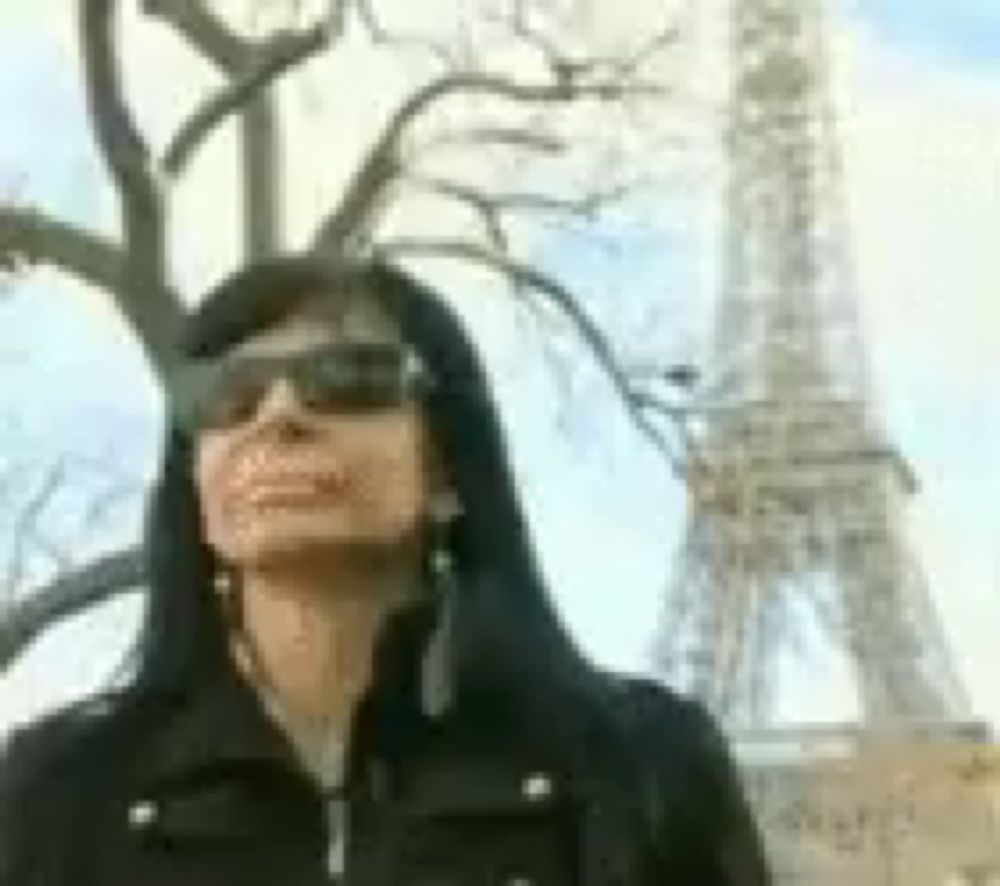 a woman wearing sunglasses and earrings is standing in front of the eiffel tower .