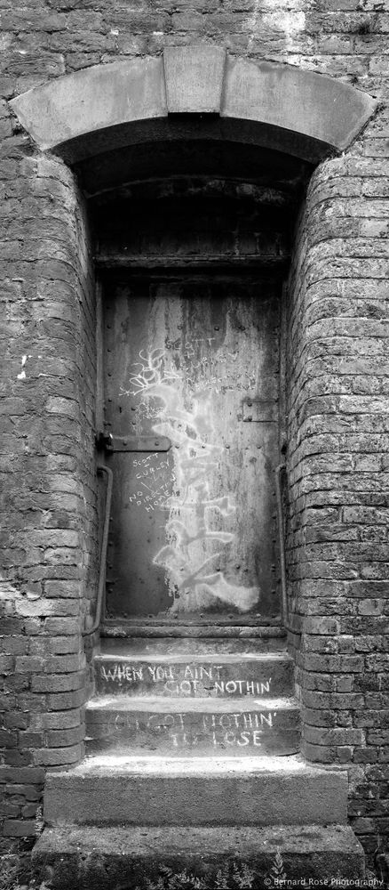 Image shows a warehouse doorway, Dublin Street, Liverpool. Graffiti on metal door and steps, brick warehouse.