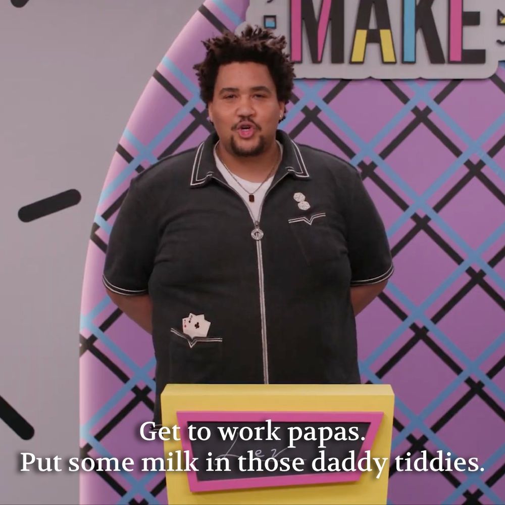 Lou Wilson stands at a lectern and says "Get to work papas. Put some milk in those daddy tiddies.