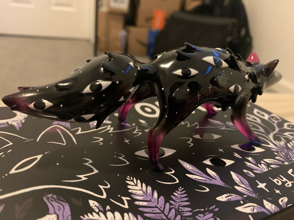 A figure of a mostly black coyote-like creature with eyes along its body. Its ears, tail, and legs are semi transparent with blue and purple coloring. This photo shows the back and right sides more clearly.