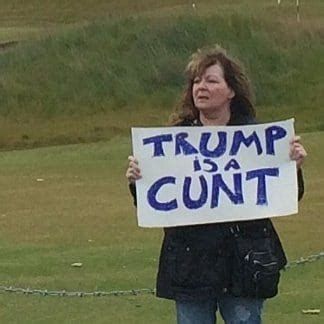 The late great Scottish comedian Jane Godley holding a sign that reads "Trump is a cunt" just beyond the edge of Trump's golf course in Scotland, during a visit Trump made in his first term