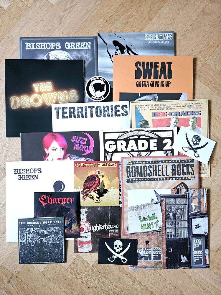 Several 12" and 7" vinyl records are put on display for promotion. All are from the punkrock label Pirates Press. The artists are The Drowns, Suzi Moon, Wonk Unit, Subhumans, Grade 2, Bishops Green, Sweat, Bombshell Rocks and more. 