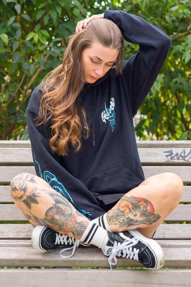 Model Mel sitting on a bench with crossed legs. Wearing the Get Dead snake hoodie. 