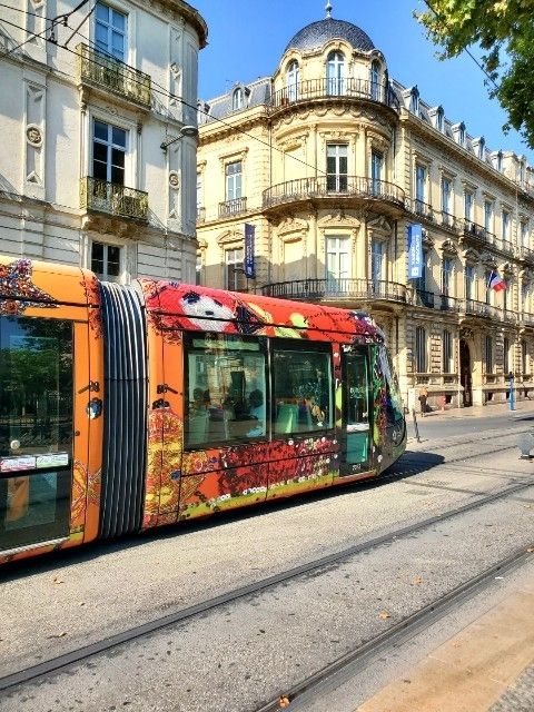 Tram covered with bright art in front of 18th century French apartment buildings
