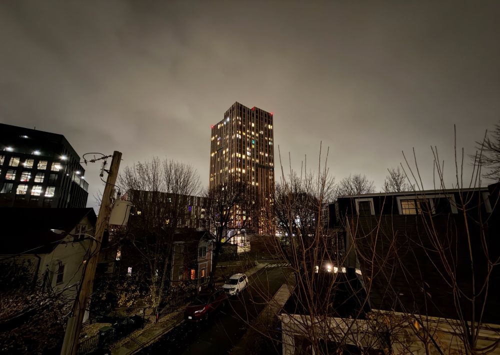 Looking at an urban skyline at night with a tall residential building in front of a clouded and backlit sky.