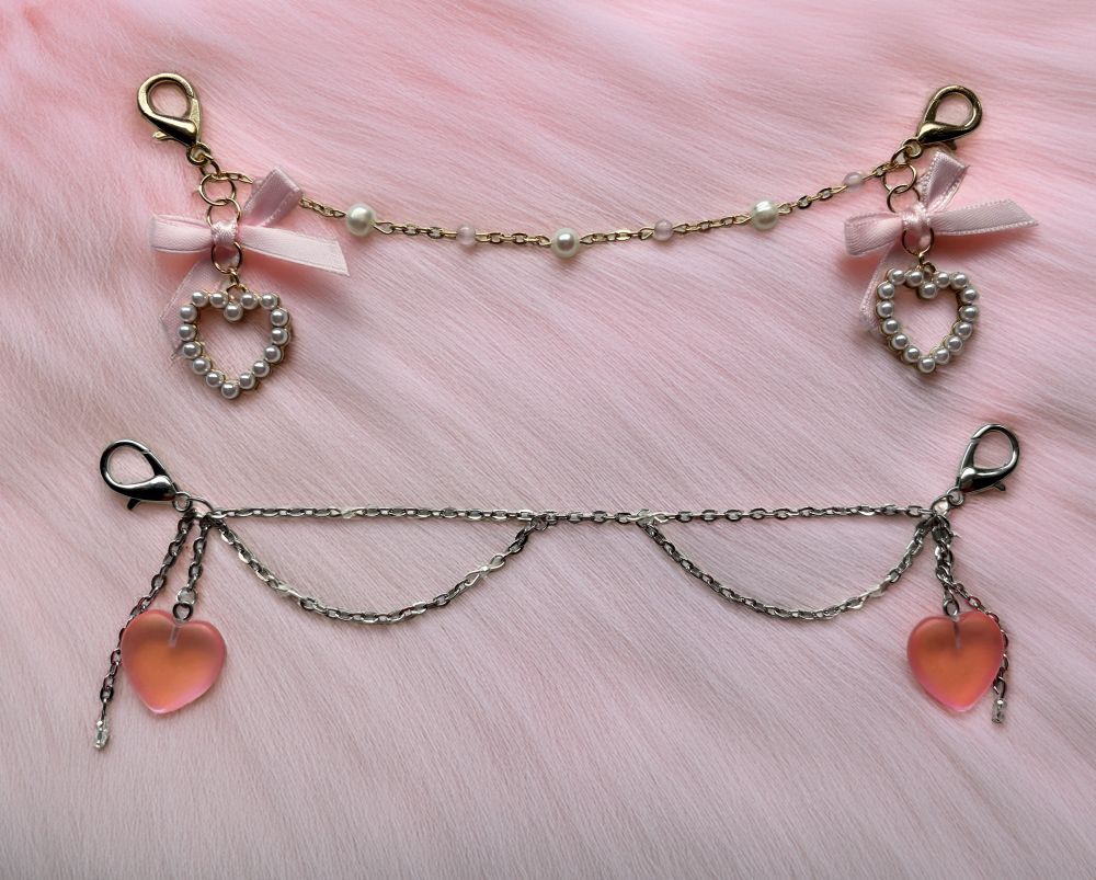 a picture of two mask chains on a pink fluffy bg. top is gold with pearl and pink beads. bottom is silver with two big hearts on each side 