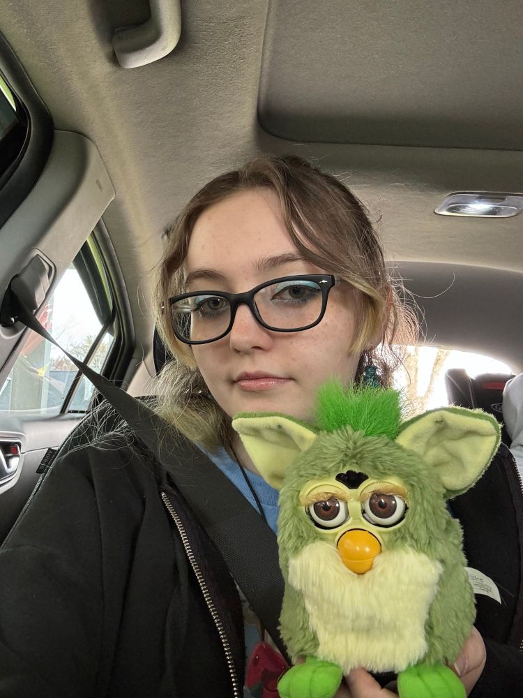 A picture of myself holding a green 1998 frog Furby with brown eyes