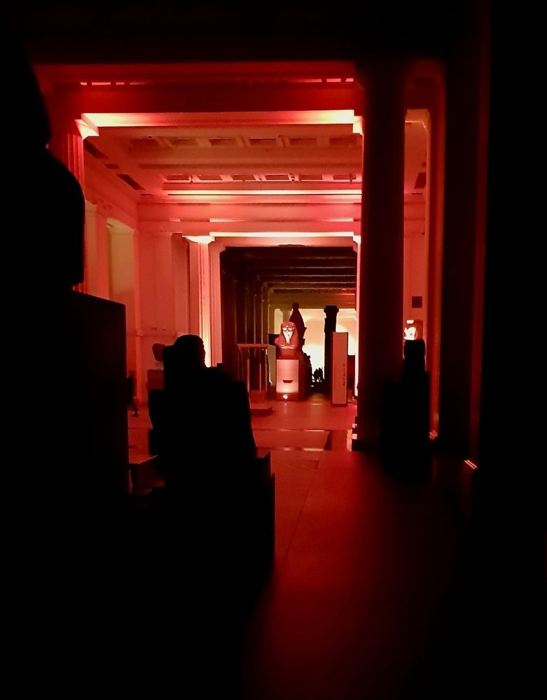 The Egyptian hall at the British Museum at night. Everything is lit with an eerie red light.