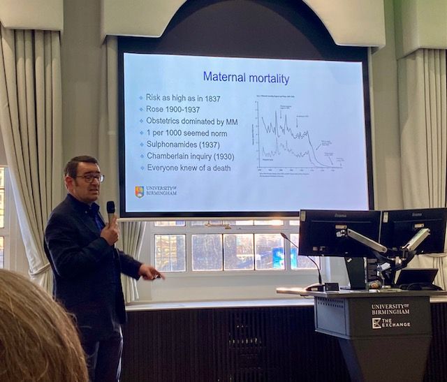 A person standing in front of presentation screen talking into microphone.