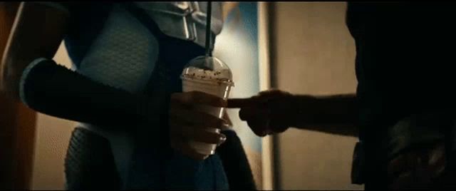 a man in a superhero costume is holding a cup of coffee and pointing at it .