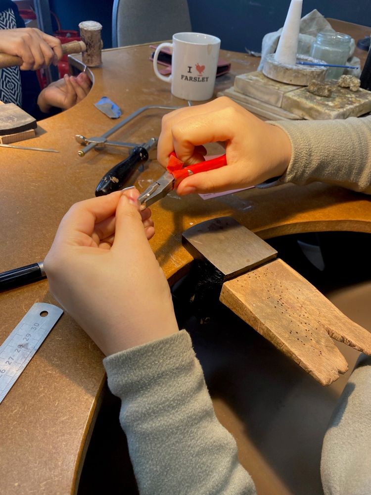 A woman's hands at a studio work station using a pair of pliers to shape a silver ring