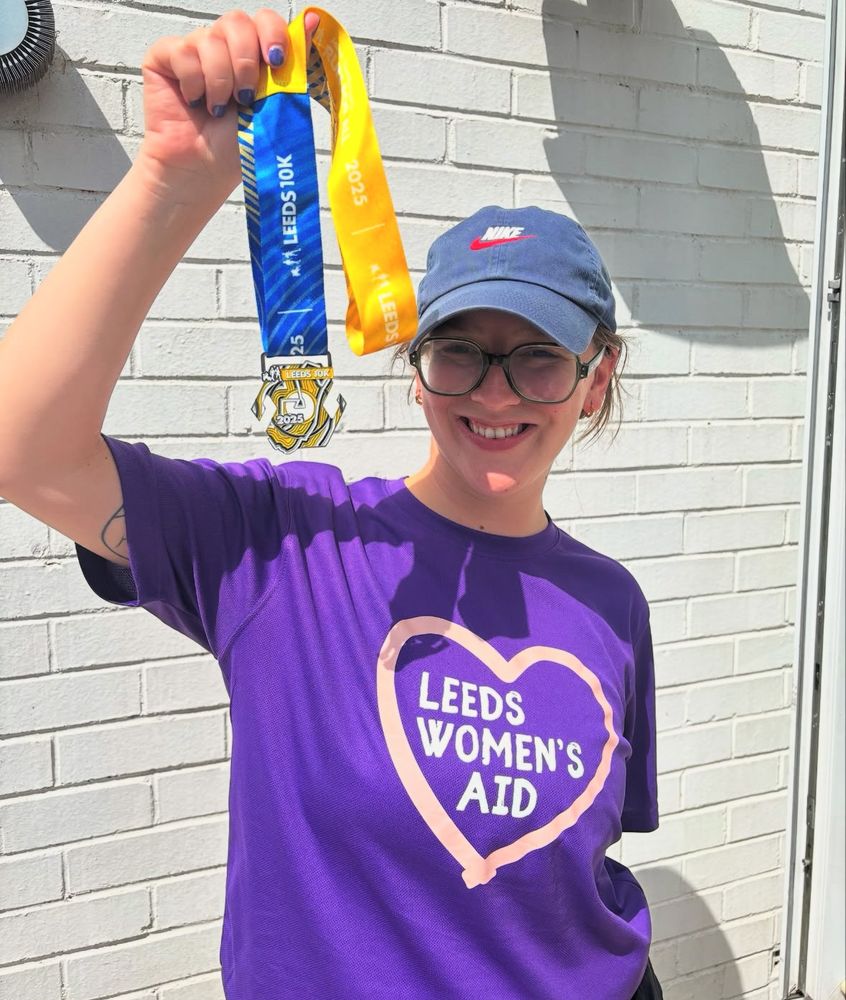 Woman  in purple lwa tshirts holding up finisher medal at end of race