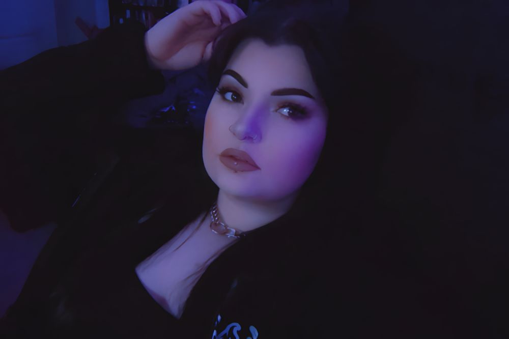 photo of a girl with dark hair and piercings posing in a hoodie and sitting in a gaming chair