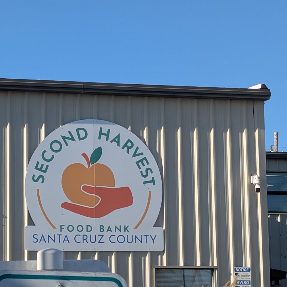 blue blue sky behind a warehouse building with a large sign of the logo a hand holding an apple Second Harvest Food Bank Santa Cruz County.