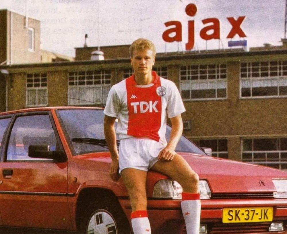 Une photo de Dennis Bergkamp jeune, portant le kit de l'Ajax d'Amsterdam, assis sur le capot d'une BX rouge