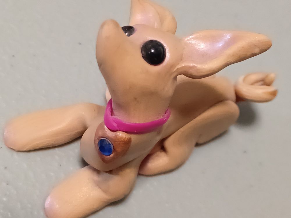 Small polymer clay dog sculpture.
Large eared light brown dog with pink collar.
Front view