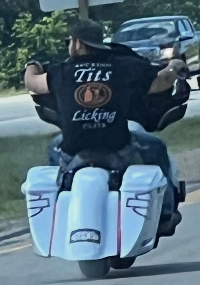 guy on a white motorcycle in a “sucking tits and licking clits” t shirt. no helmet