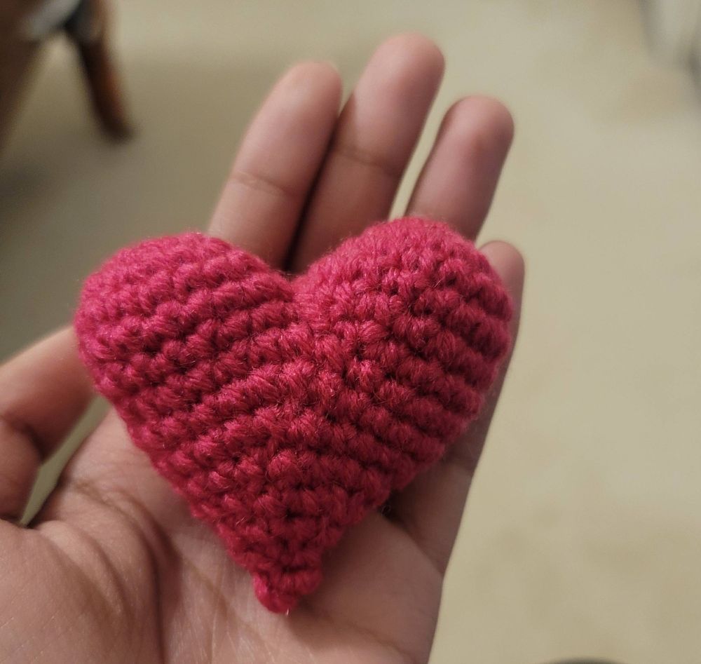 a crocheted heart in my hand with magenta yarn