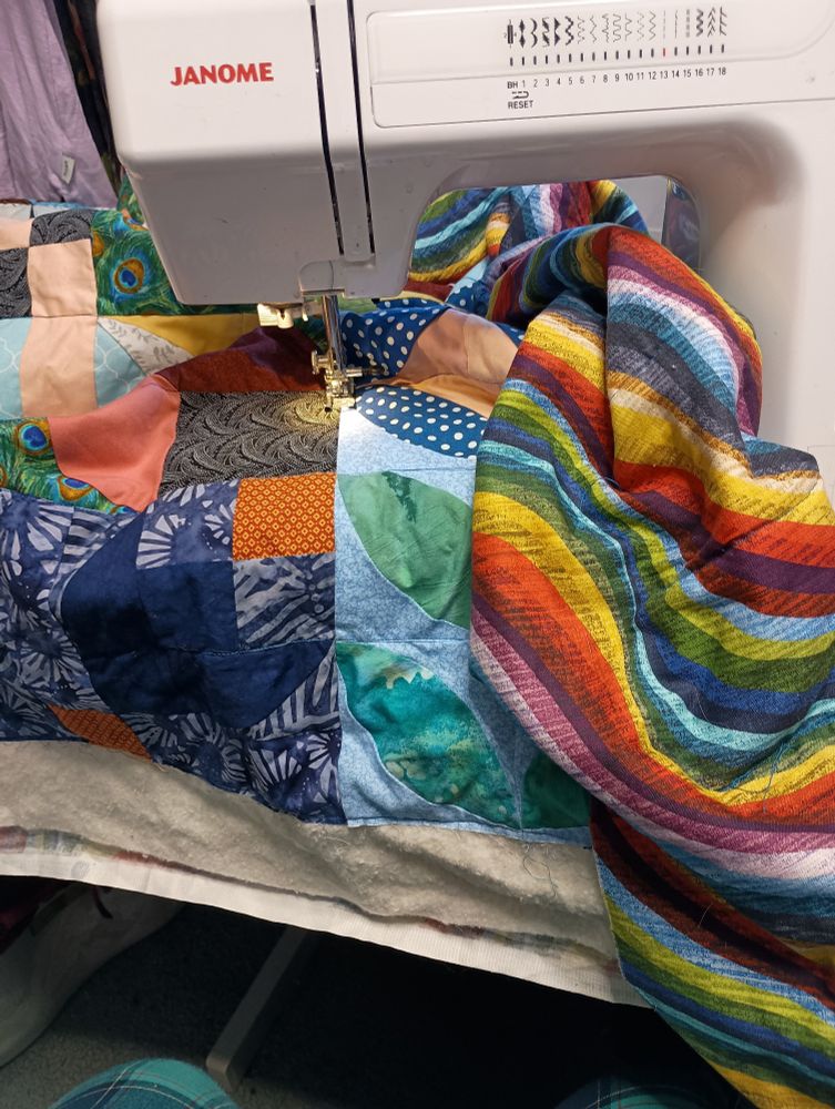 An extremely colorful quilt is under the needle of a janome sewing machine.