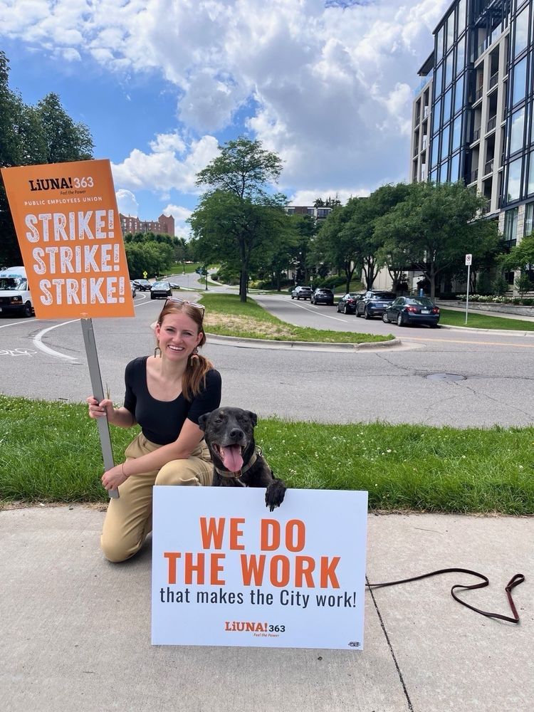 Katie Cashman and a dog pose with LIUNA signs on the picket line 