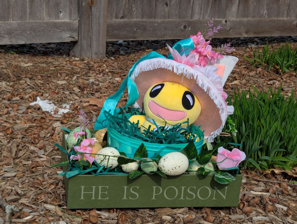 Topato dressed in a fancy little Easter getup sitting is a box adorned by pretty eggs and flowers. The box reads HE IS POISON