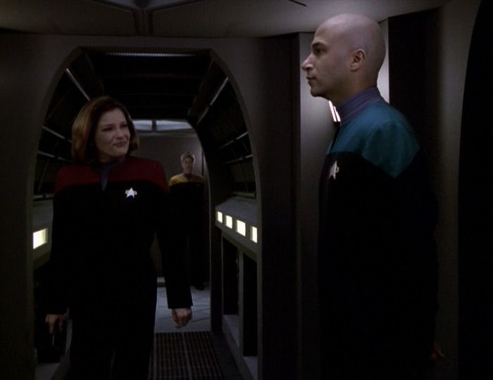Captain Janeway strolling through the bowels of the ship on deck 15 walking towards a crewman in a science uniform who is standing at attention