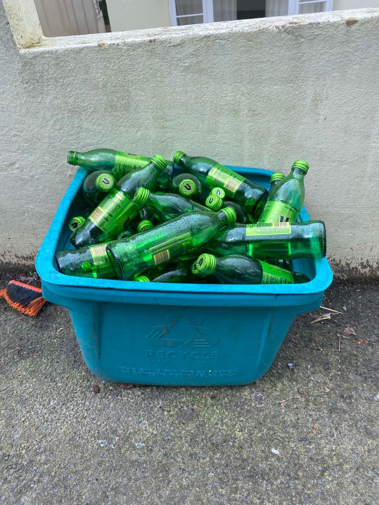 A recycling bin full of empty V energy glass drink bottles.