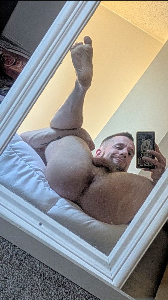 Mirror selfie, laying back on bed. Holding leg in the air showing hole and balls. 