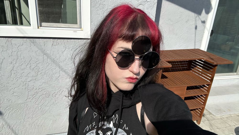 ellen saucysphinx wearing sunglasses with three round lenses outside of a house, the lighting is high contrast 