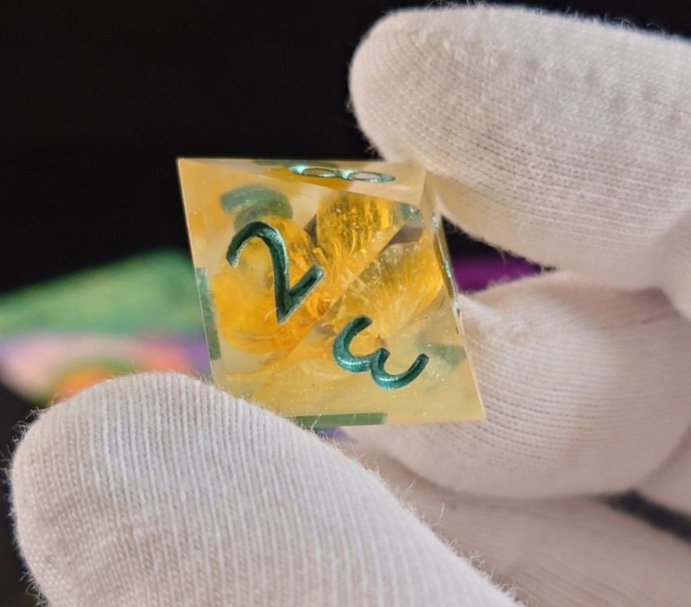 a a transparent eight-sided die with a yellow buttercup and green numbers