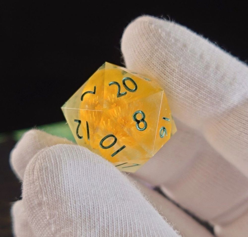 a a transparent twenty-sided die with a yellow buttercup and green numbers