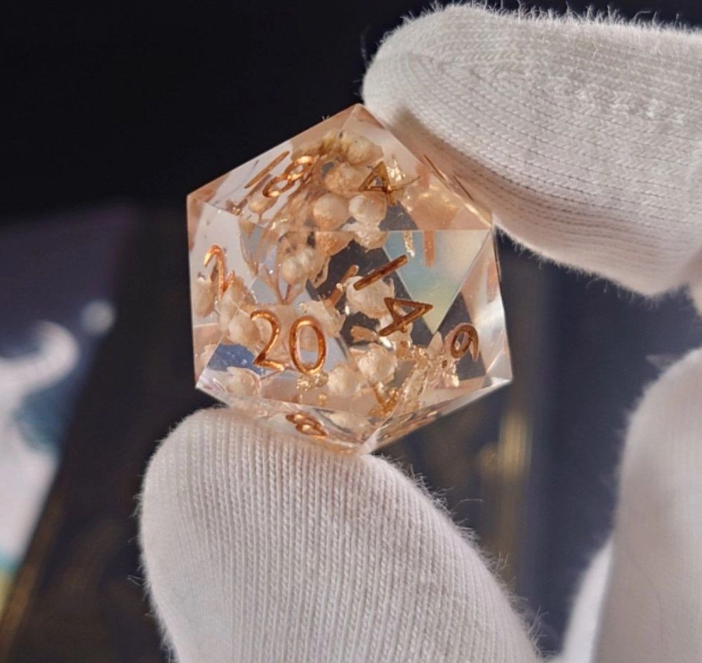 a hand holding a 20-sided die with white flowers inside